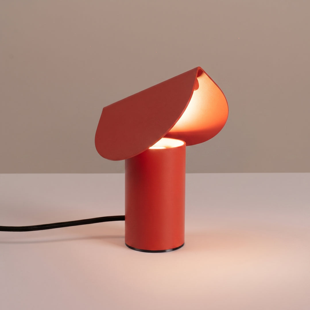 Lampe à poser BISCUIT rouge allumée, sur une table