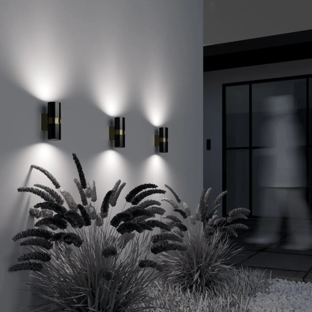 Trois appliques extérieure bowery cylindre double en métal noir avec accents dorés éclairent un espace moderne extérieur