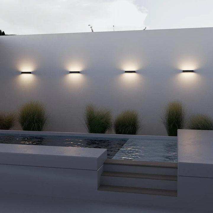 Quatre appliques extérieures barre horizontale en acier noir minimalistes avec une lumière chaude sur mur blanc