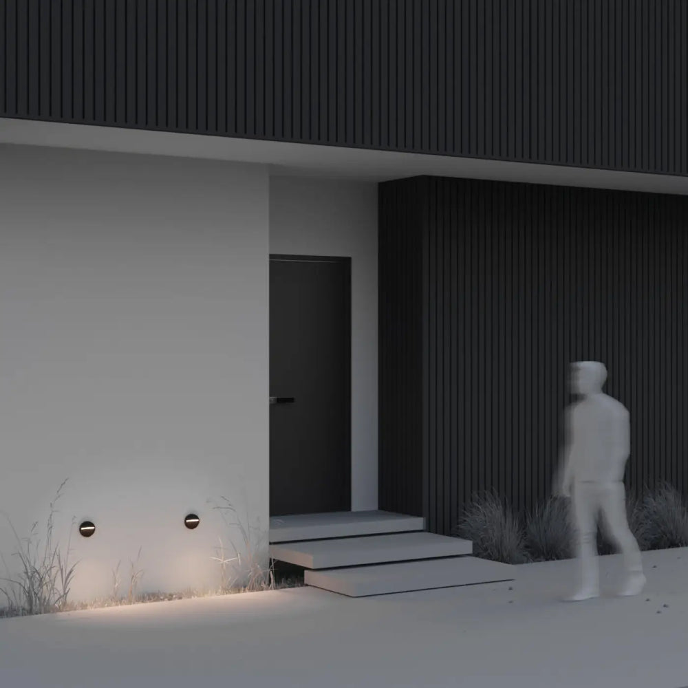 Applique extérieure balise ronde noire minimaliste avec lumière douce éclairant la base d’une maison moderne