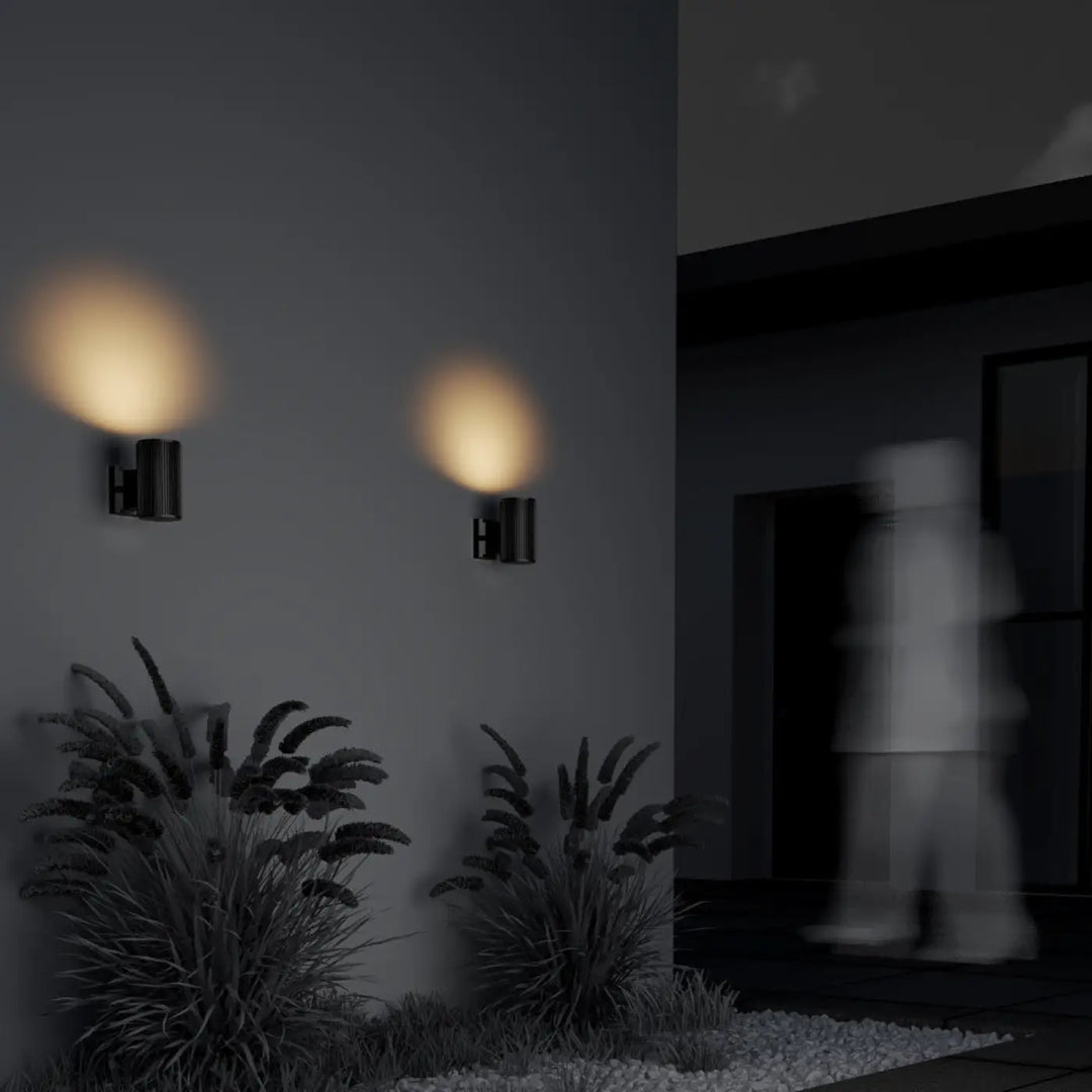 Deux appliques extérieures rando noirs cylindre étanche diffusant une lumière chaude sur un mur gris foncé