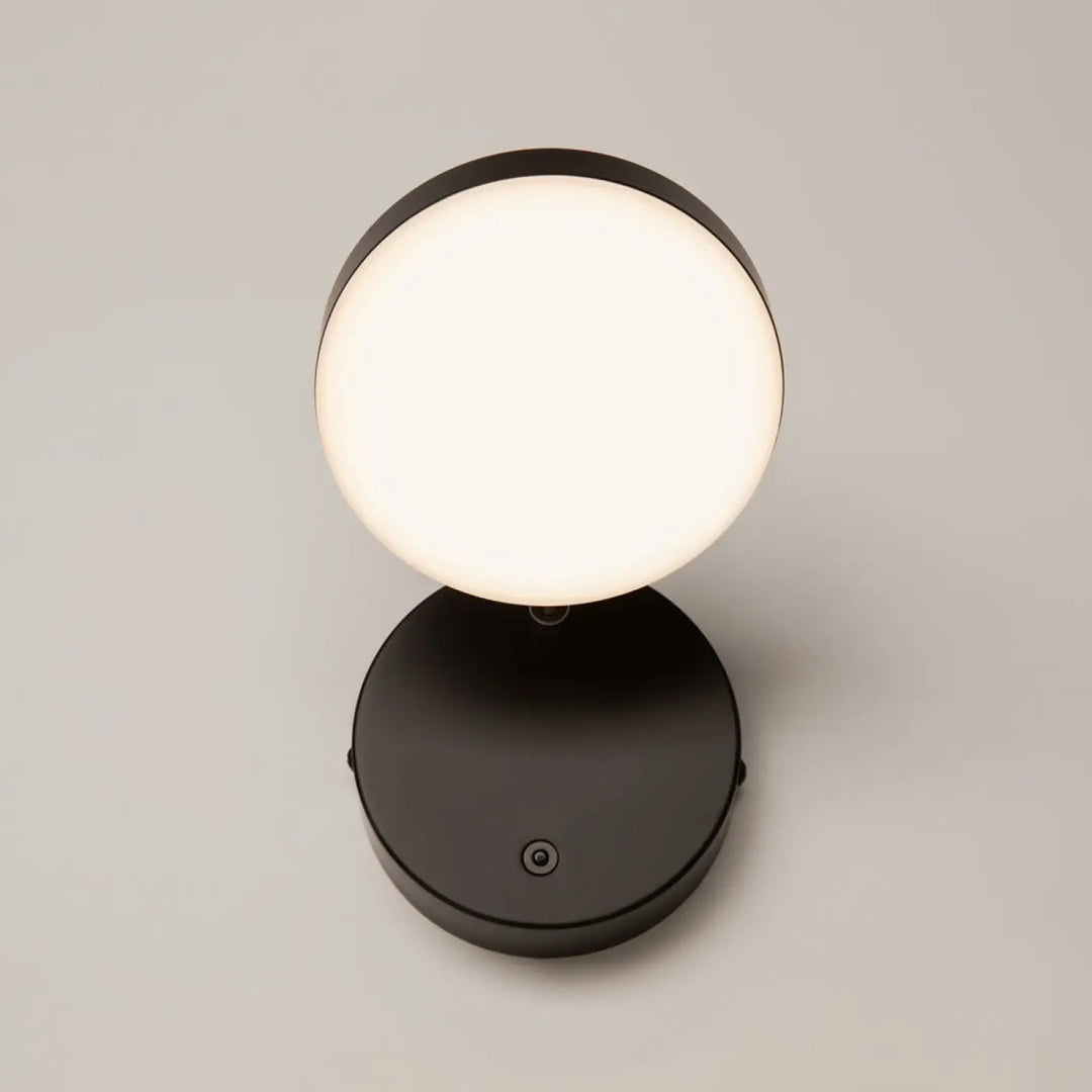 Applique murale fad liseuse métal noir avec tête ronde orientable et lumière blanche douce sur une table moderne