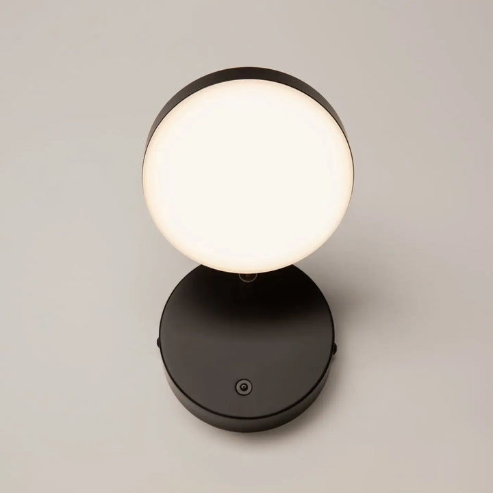 Applique murale fad liseuse métal noir avec tête ronde orientable et lumière blanche douce sur une table moderne