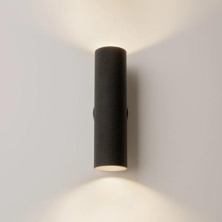 Applique murale artisan noire cylindrique avec surface texturée et éclairage d’accent chaleureux et focalisé