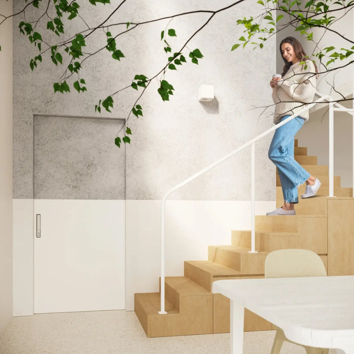 Femme en pull crème et jean debout sur escalier en bois devant applique murale céramique moderne subani