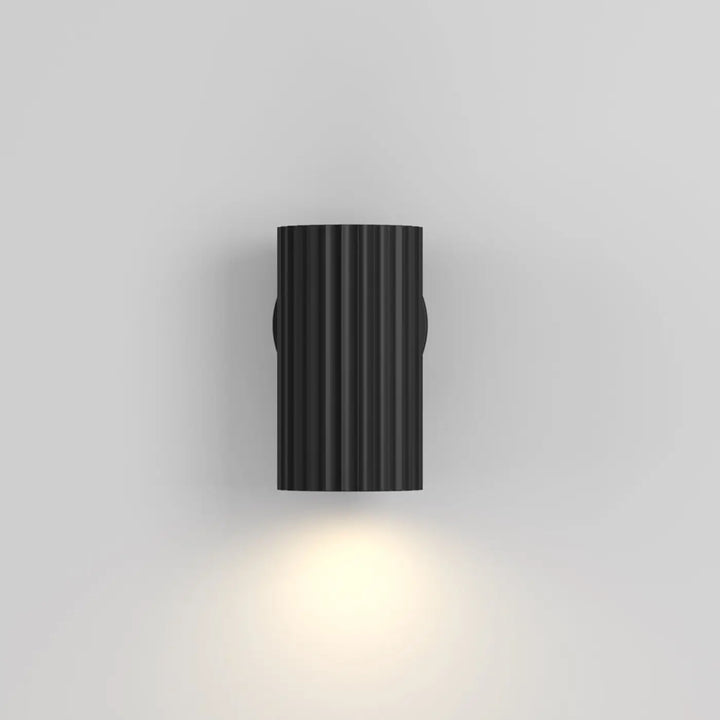 Applique murale calipso cylindre cannelé noir avec lumière chaude projetée verticalement pour intérieur moderne