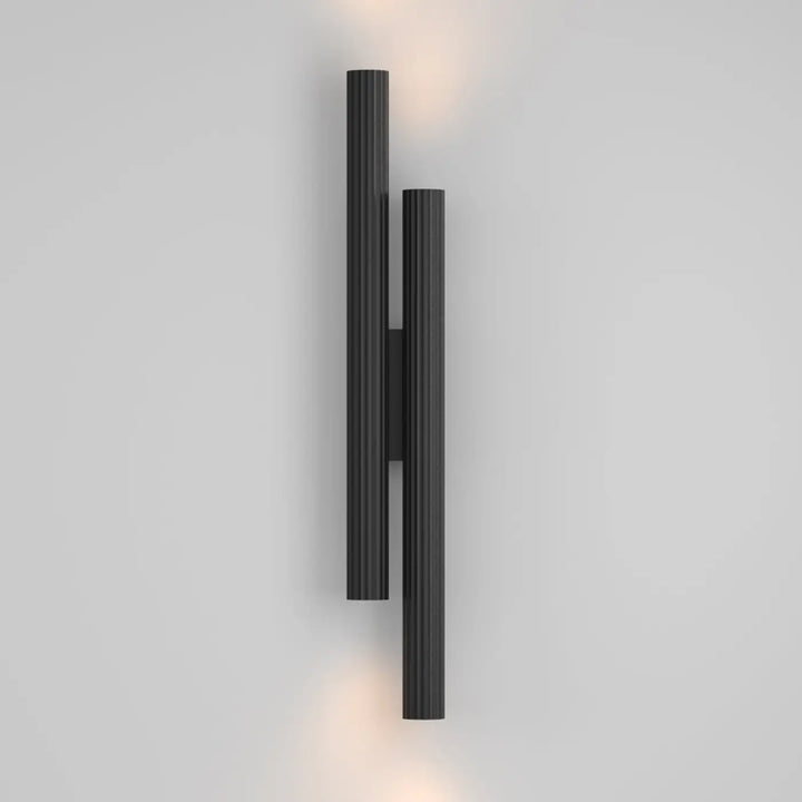 Applique murale calipso led linéaire noire avec deux colonnes cannelées diffusant une lumière chaude elegante