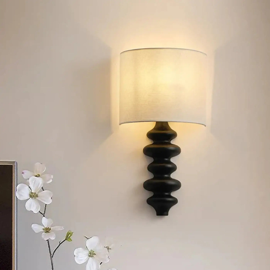 Applique murale en fer forgé noir avec abat-jour cylindrique en tissu écru offrant une lumière chaleureuse minimaliste