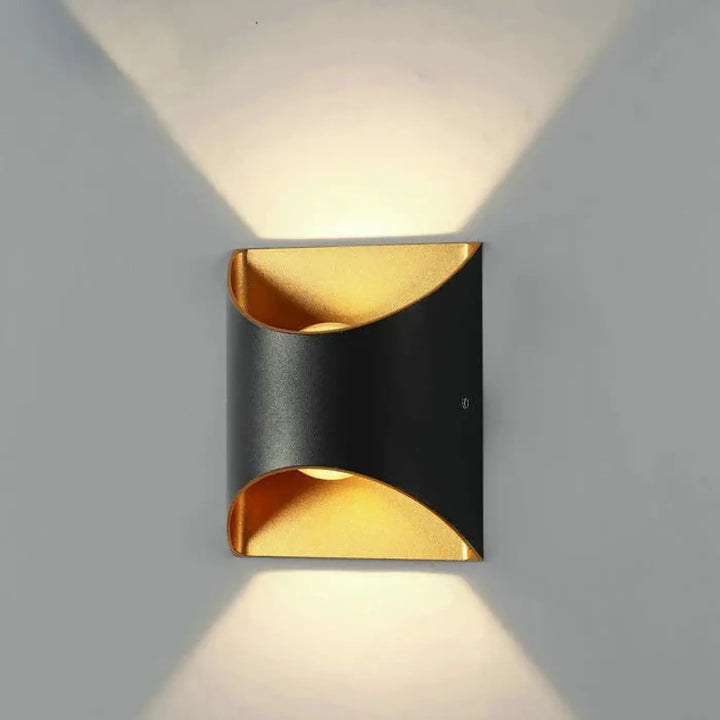 Applique murale moderne noire et dorée avec design courbé diffusant une lumière chaude dans deux directions