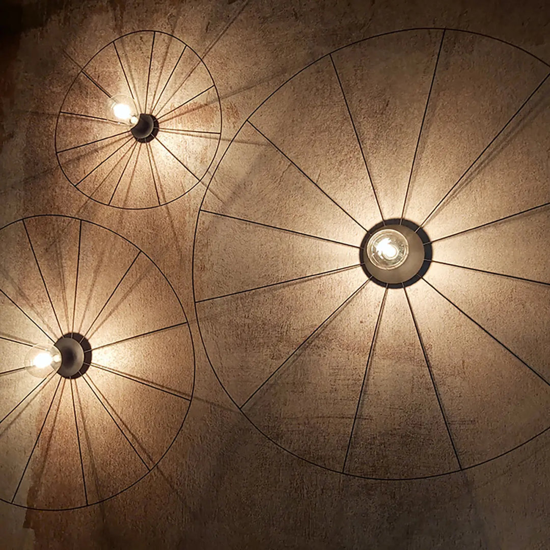 Trois lampes eskola circulaires noires avec ampoules apparentes et design à rayons montées sur murs texturés