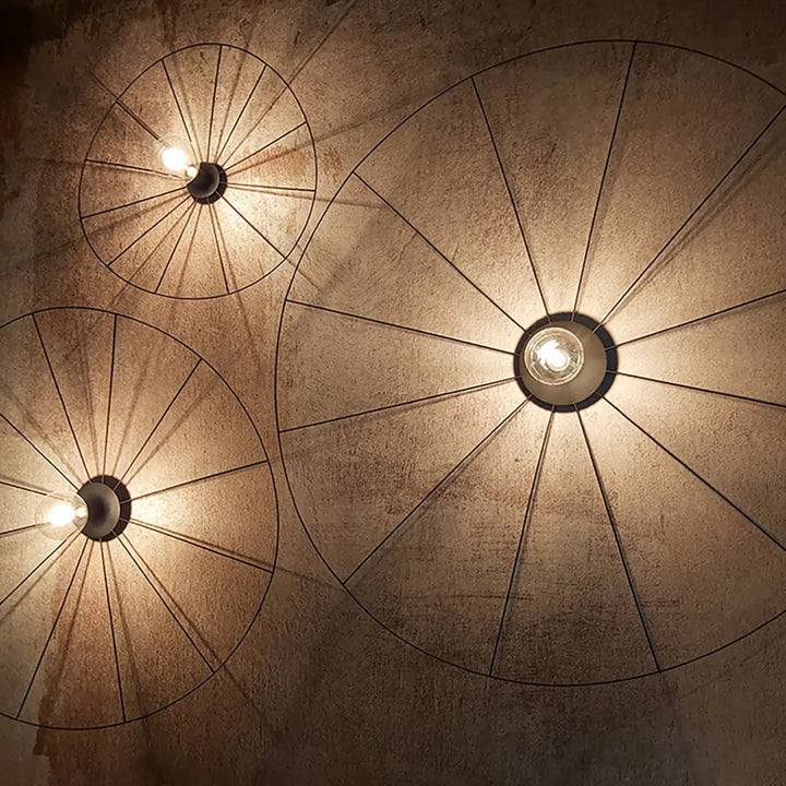 Trois lampes eskola circulaires noires avec ampoules apparentes et design à rayons montées sur murs texturés