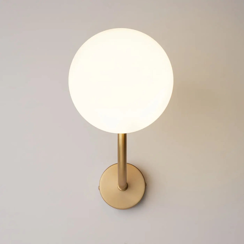 Applique murale rendez vous avec globe en verre blanc givré et bras doré minimaliste en laiton élégant