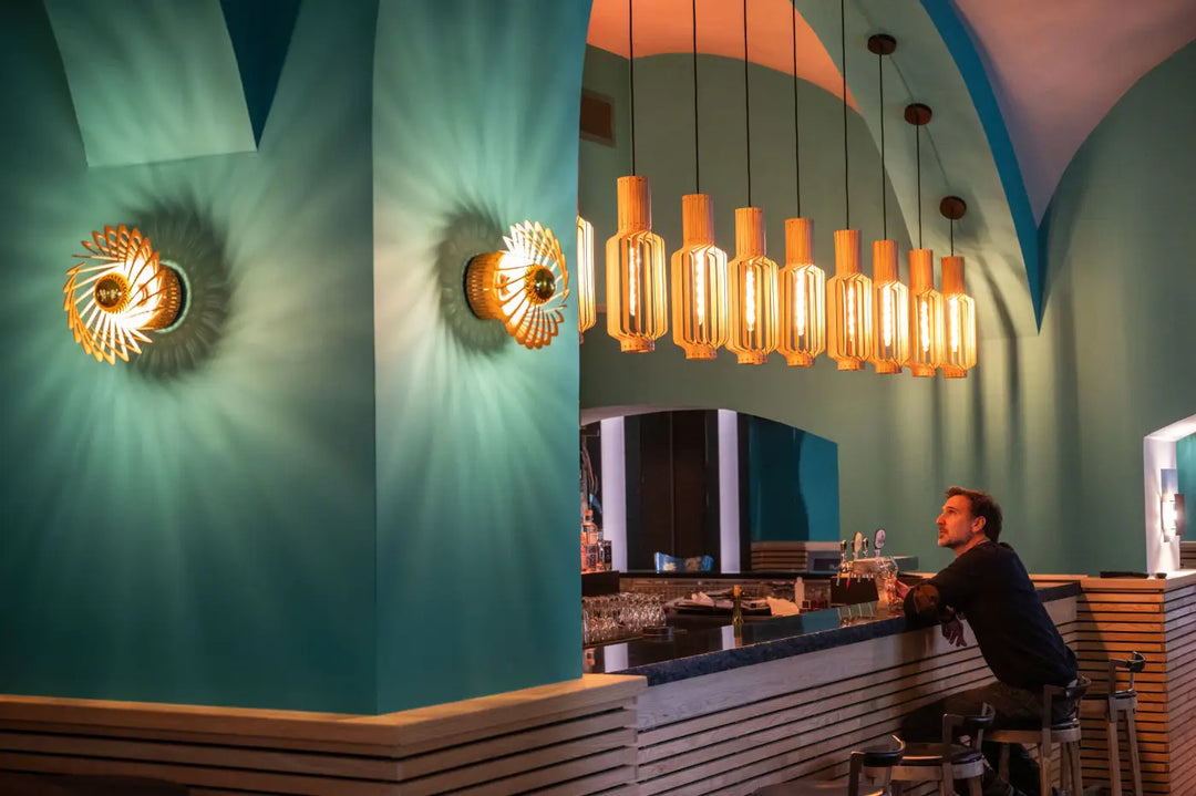 L’applique murale pianumayo style soleil doré avec abat-jour ambre suspendue au-dessus d’un bar bleu sarcelle bois fsc
