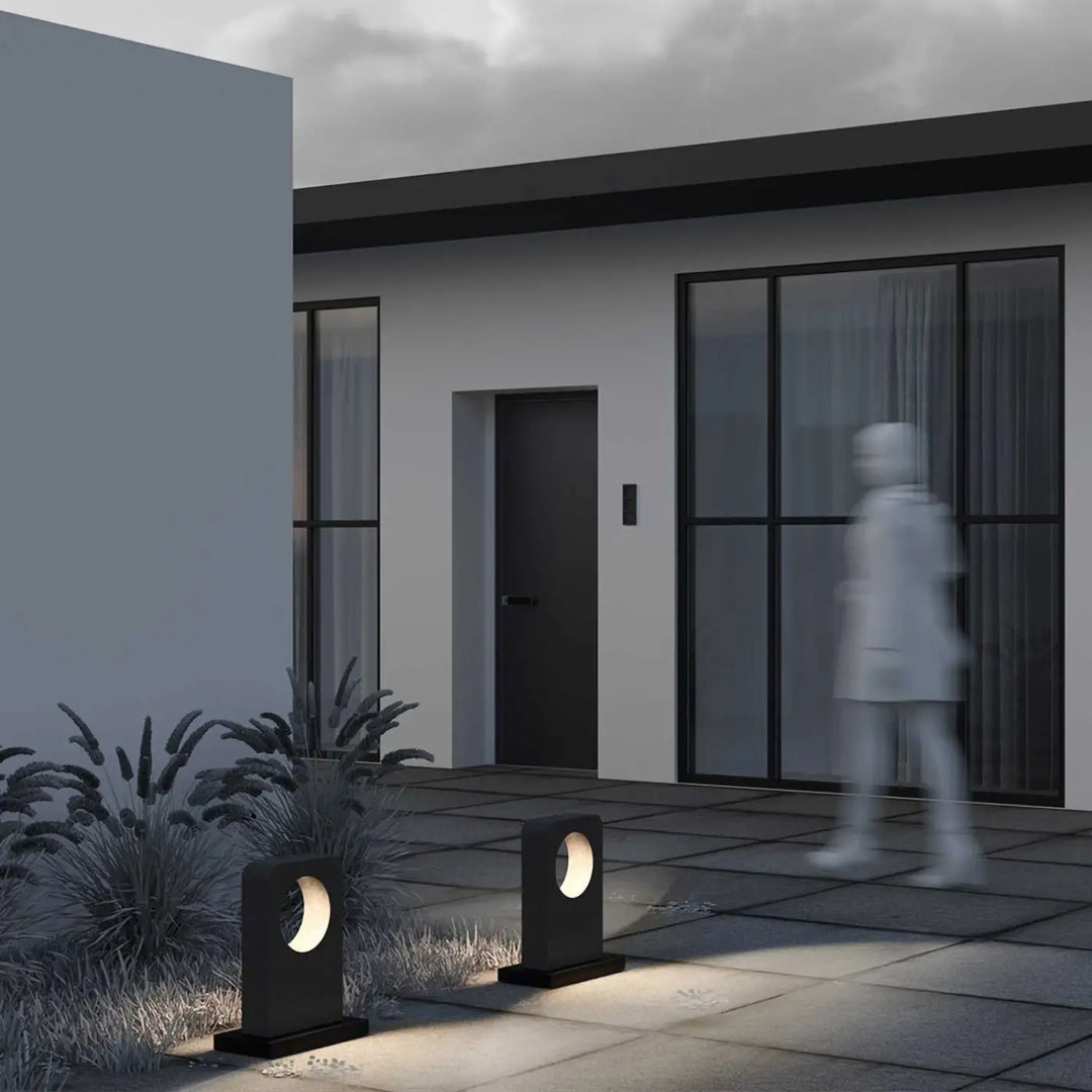 Borne extérieure en béton gris moderne avec découpes circulaires diffusant une lumière chaude le long d une allée