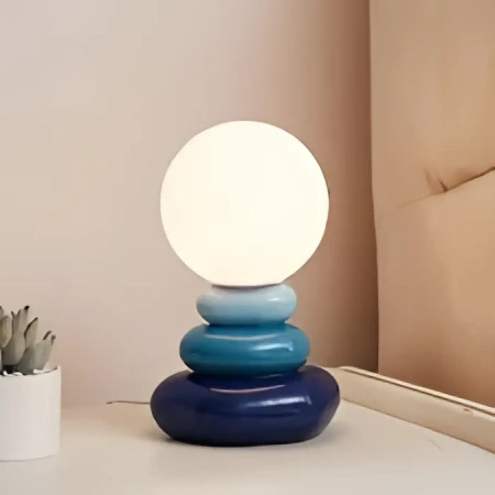 Lampe de chevet hestia avec design galets empilés et base circulaire bleue surmontée dune sphère lumineuse blanche