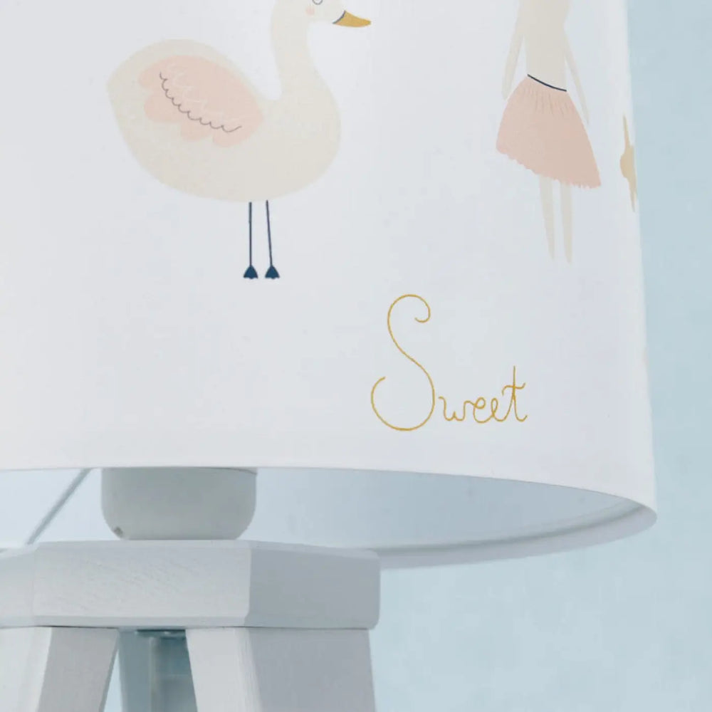 Lampe de table blanc avec abat-jour pastel illustrant un cygne et une fille en jupe orné de sweet en doré pour chevet enfant bois motifs animaliers
