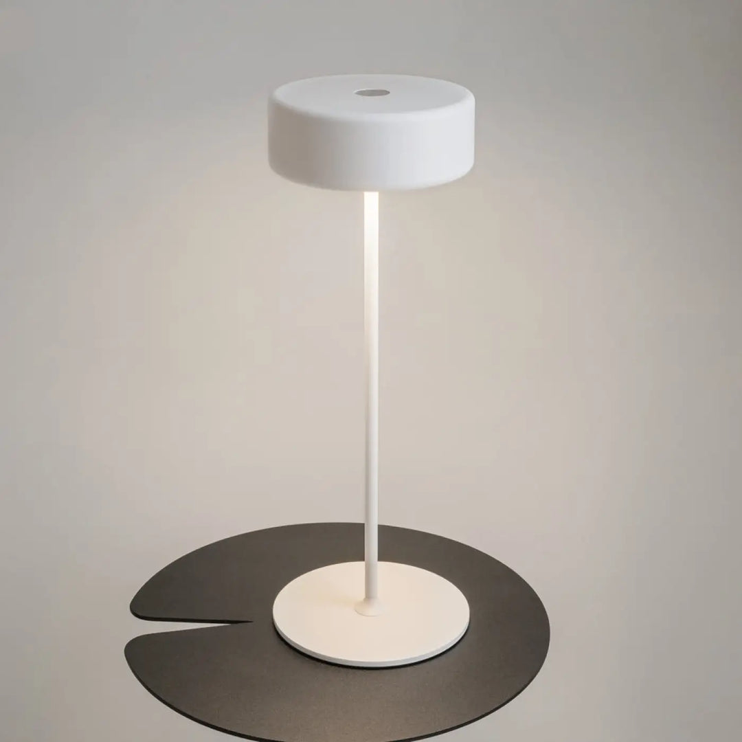 Lampe de chevet blanche design épuré avec abat-jour cylindrique et pied aluminium sur plateforme feuille pour salle à manger trois finitions