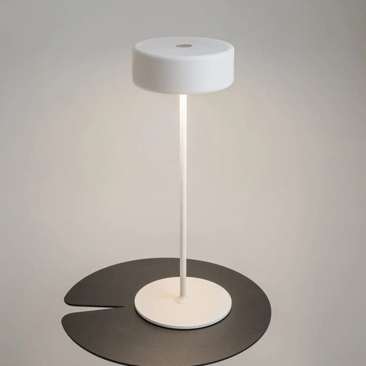 Lampe de chevet blanche design épuré avec abat-jour cylindrique et pied aluminium sur plateforme feuille pour salle à manger trois finitions