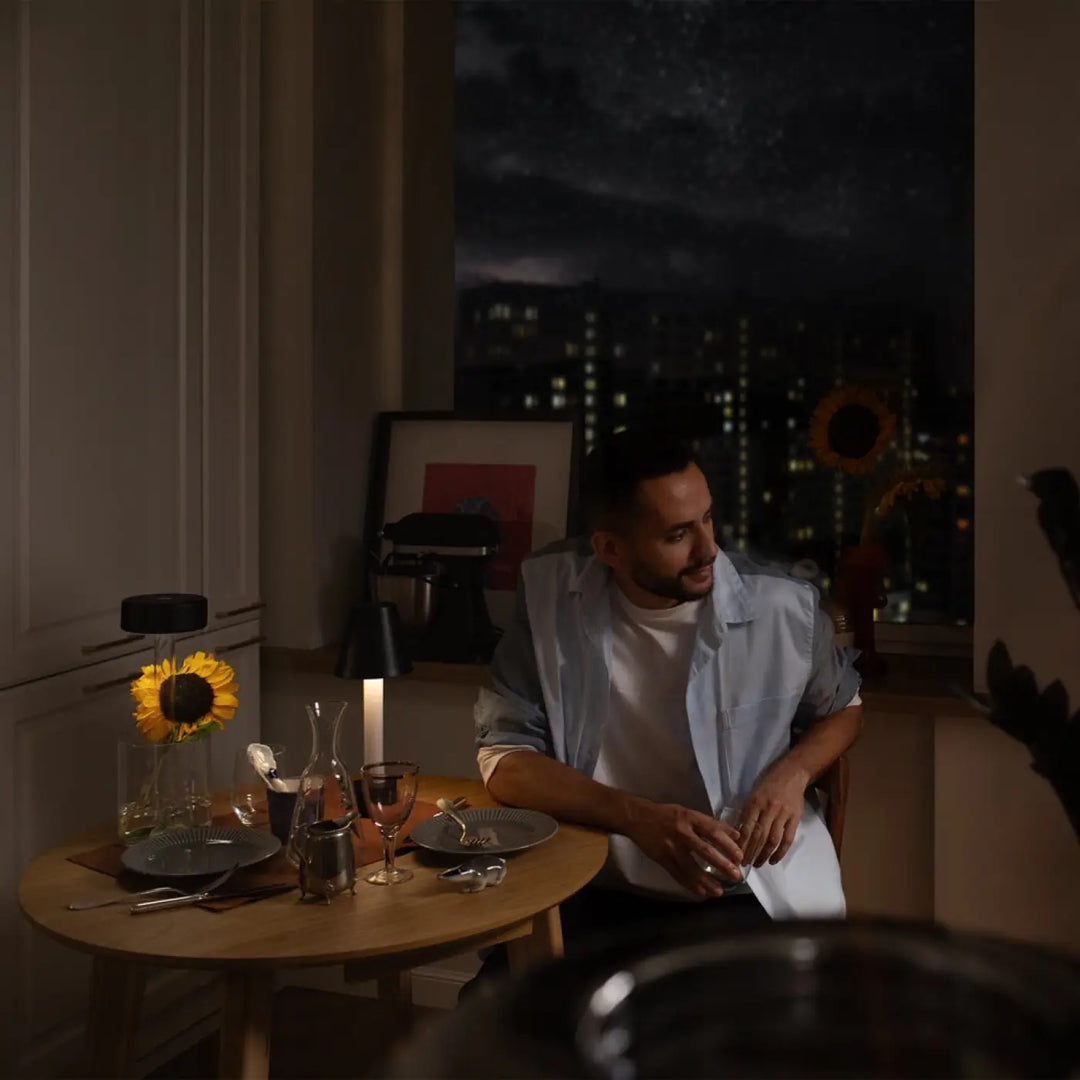 Un homme en chemise bleu clair tient un verre près dune lampe de chevet vase à lumière led dimmable et batterie rechargeable