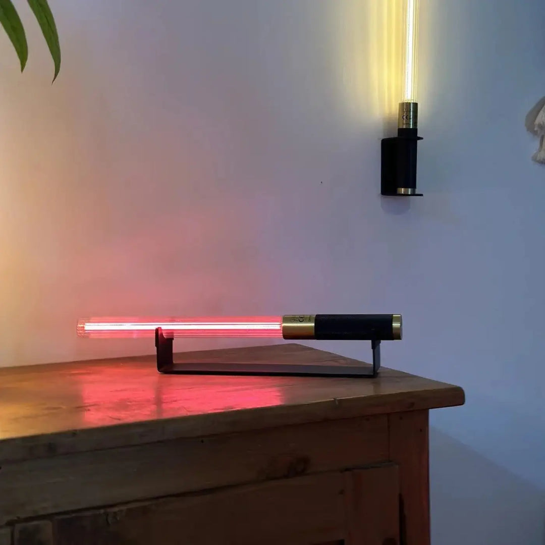 Lampe de chevet hélios avec objet lumineux sabre laser néon rouge et accents noirs et dorés sur surface en bois