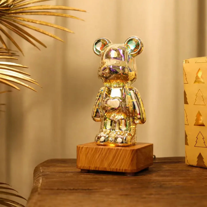 Lampe ourson décorative en figurine dorée irisée avec motif cœur, posée sur base en bois, offrant effets lumineux multicolores