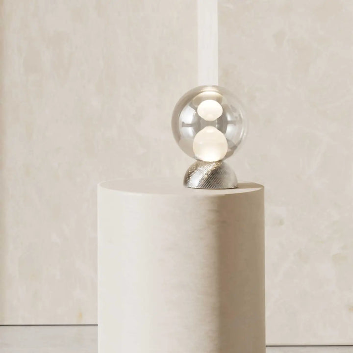 Lampe de chevet poser charm avec sphère lumineuse cachée dans un globe compact en verre transparent et base argentée texturée