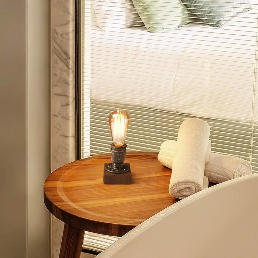 Lampe de table filamenta industrielle avec ampoule filament ambre sur base metal foncé posée sur table décorative industrielle en bois