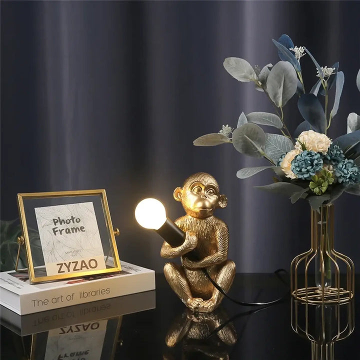 Lampe de table zaboo avec singe assis doré tenant une ampoule allumée sculpturale singe assis pour bureau
