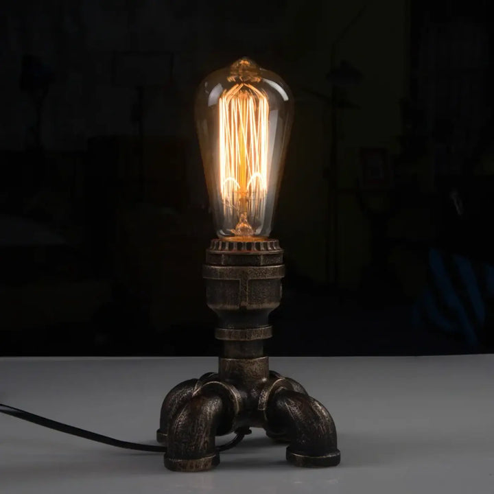 Lampe de table forge en style industriel avec ampoule à filament dans verre transparent sur base métallique sombre pour décoration intérieure chaleureuse