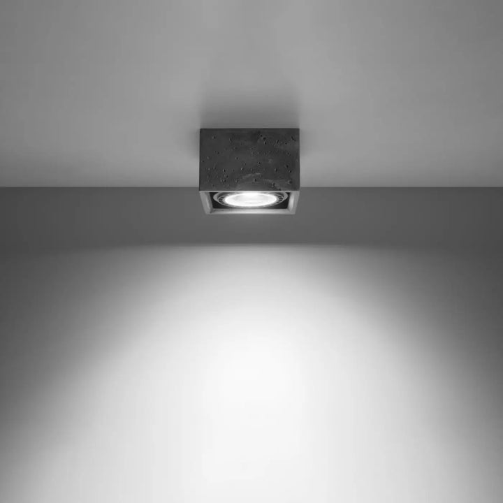 Luminaire plafonnier béton quatro carré avec ampoule circulaire encastrée émettant une lumière blanche vive