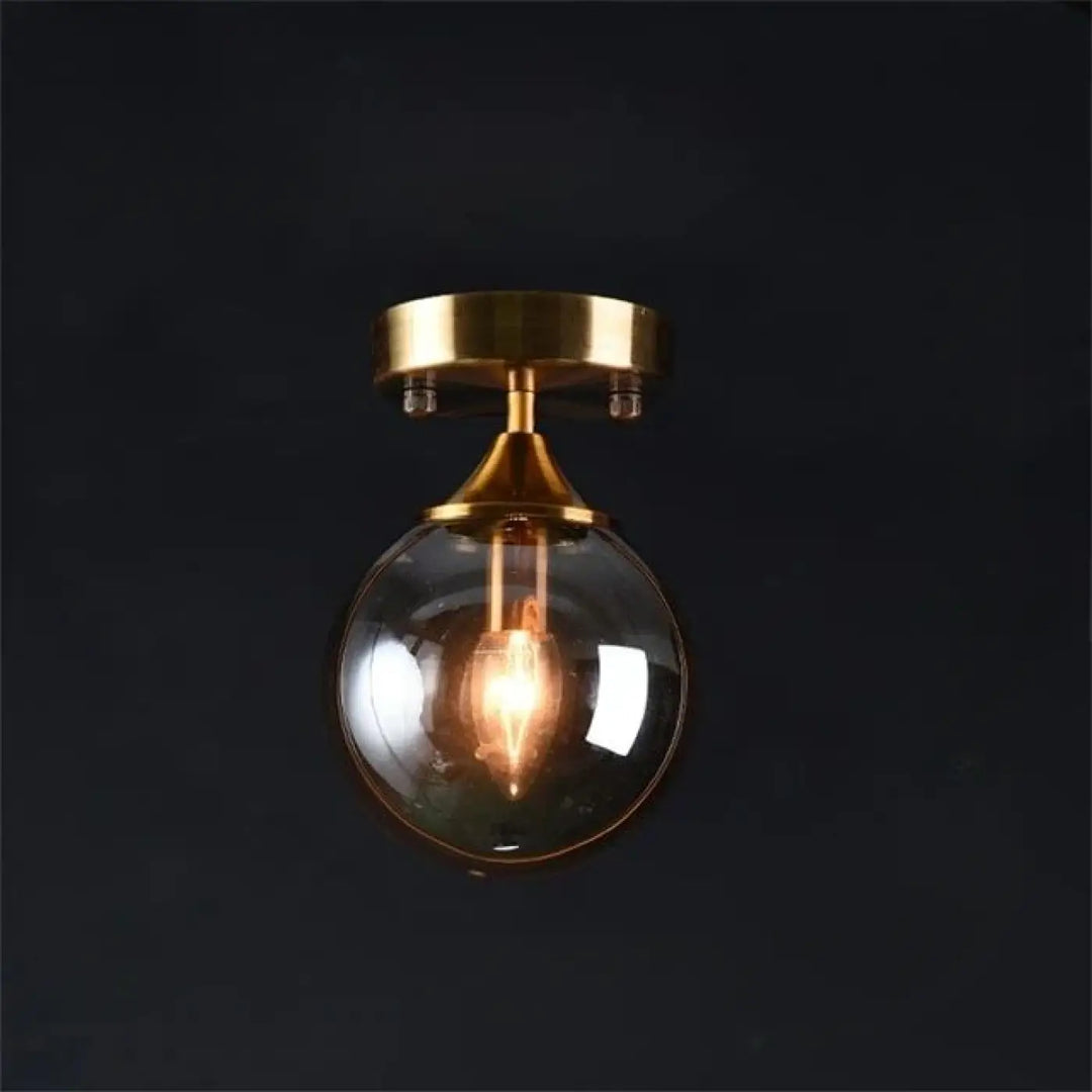 Plafonnier chic boule lumineuse en verre sphérique avec finition laiton et anneau doré visible sur luminaire orbane