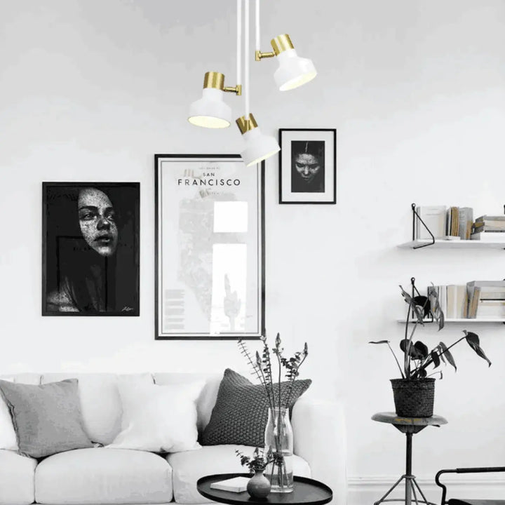 Plafonnier dorothy blanc moderne en finition or avec trois abat-jours en céramique blanche au-dessus d’un salon minimaliste