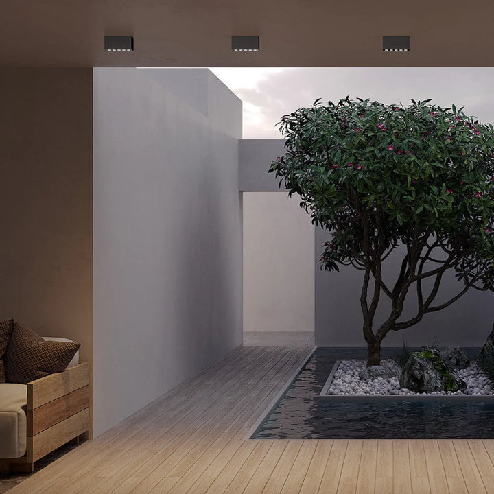 Luminaire extérieur ares avec plafonnier extérieur en métal graphite près d’un arbre aux fleurs roses dans un jardin minimaliste