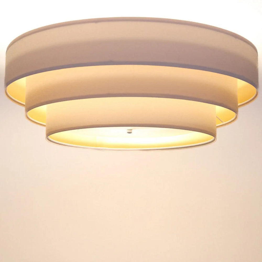 Plafonnier rond blanc doré triniti veloursstoff avec trois abat-jours circulaires en tissu beige émettant une lumière chaude