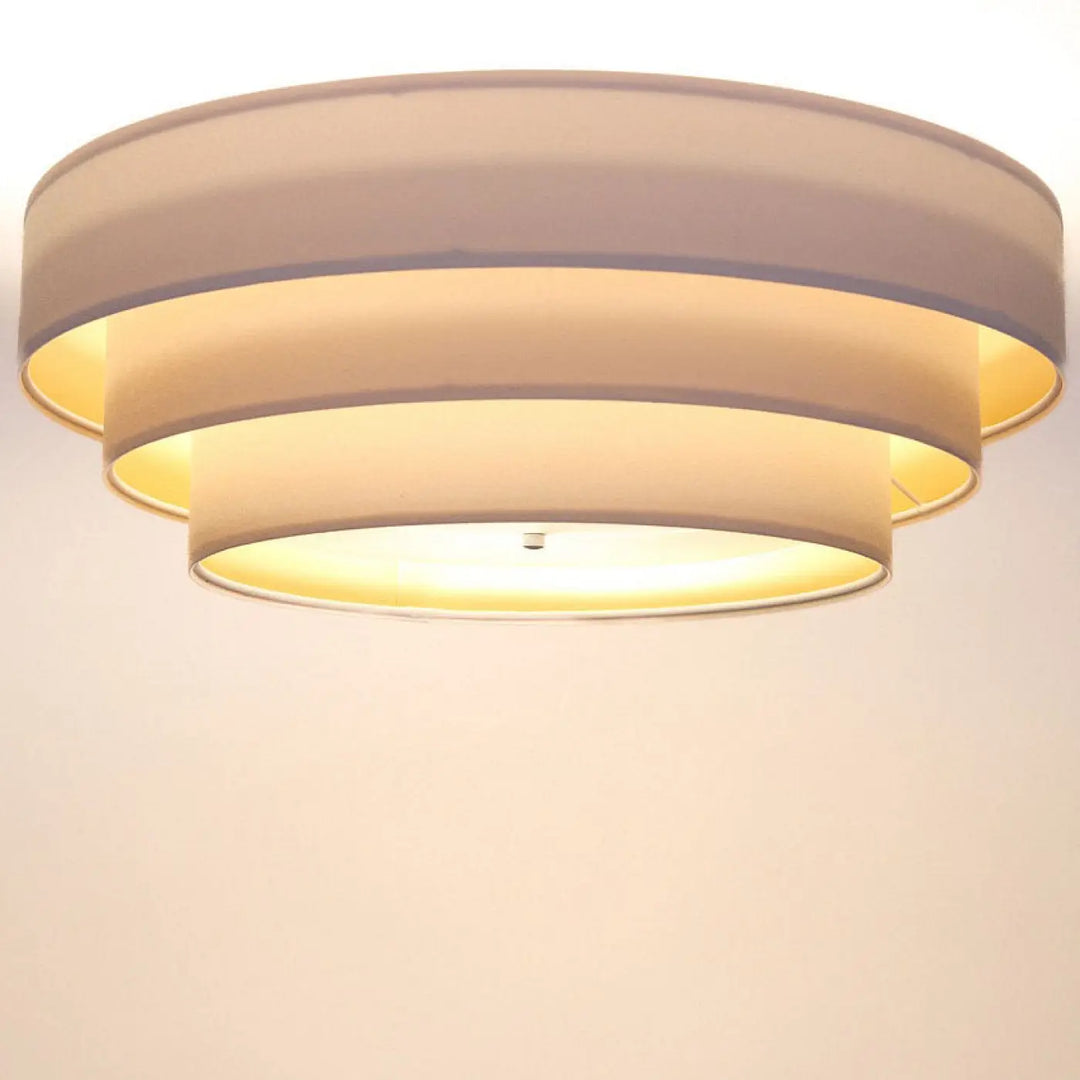 Plafonnier rond blanc doré triniti veloursstoff avec trois abat-jours circulaires en tissu beige émettant une lumière chaude