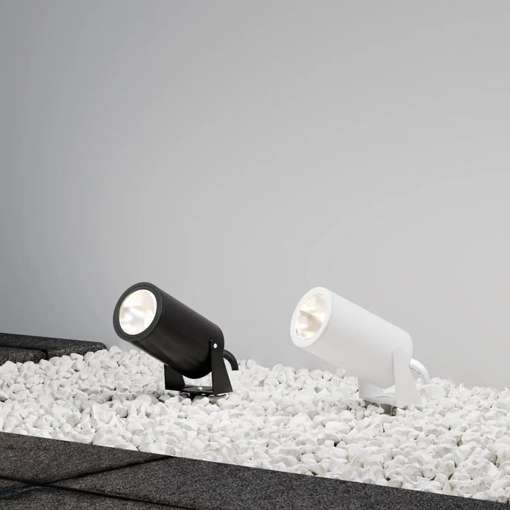 Deux spots piquet extérieur cylindriques modernes, noir et blanc, avec tête orientable, posés sur des galets blancs
