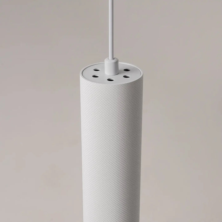 Suspension artisan blanche cylindrique en tissu texturé avec trous de ventilation au-dessus d’une table