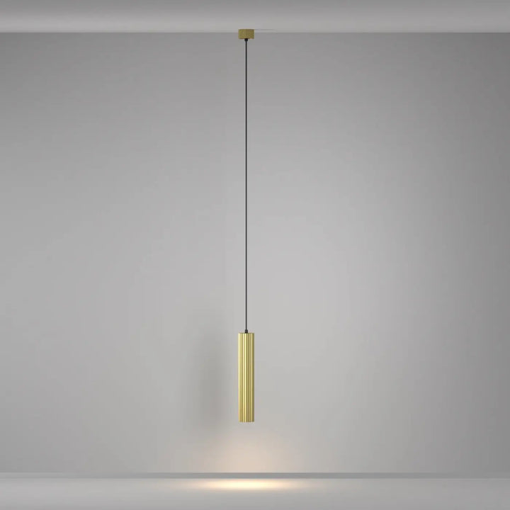 Suspension luminaire calipso tube au-dessus d’un îlot en métal brossé doré avec cordon noir fin et rainures verticales
