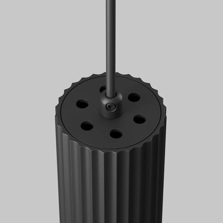 Suspension luminaire calipso tube noir cylindrique avec rainures verticales et dessus perforé au-dessus d’un îlot