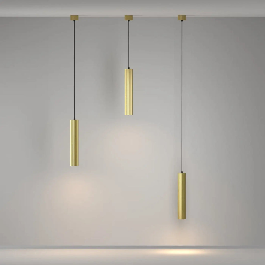 Suspension luminaire calipso tube en or avec rainures verticales suspendue au-dessus d’un îlot par des cordons noirs