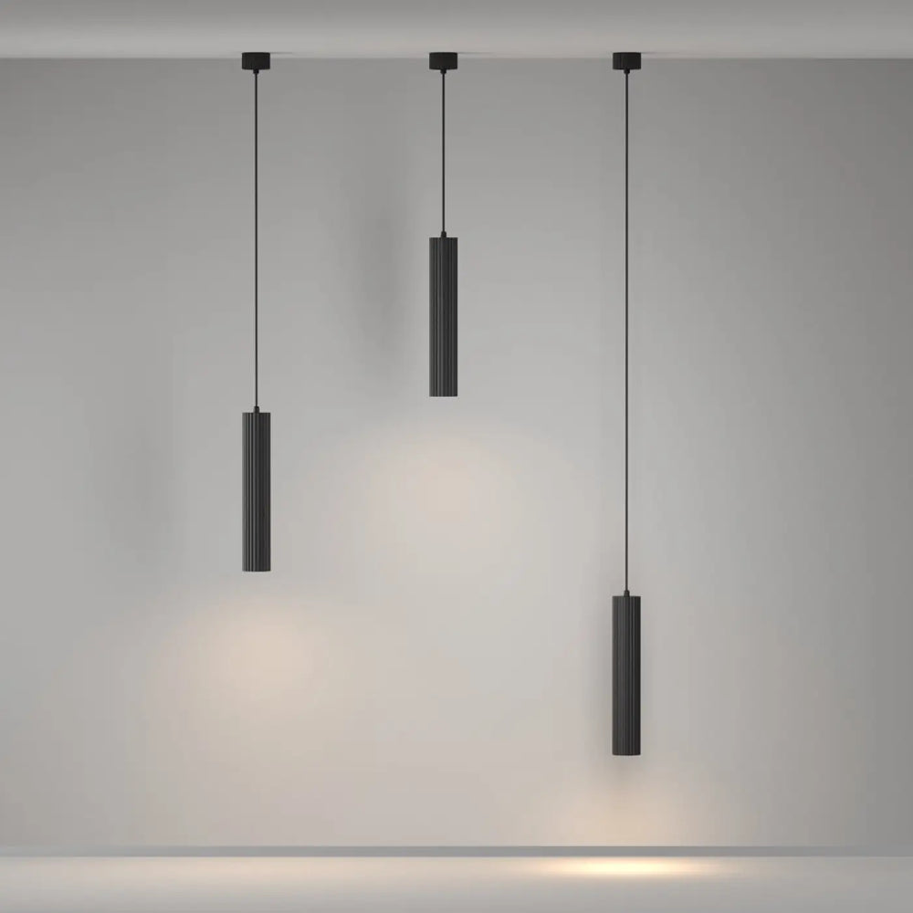 Suspension luminaire calipso tube noire en cylindre avec rainures verticales émettant une lumière chaude au-dessus d’un îlot