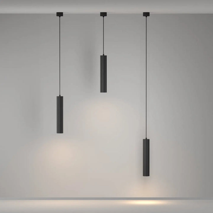 Suspension luminaire calipso tube noire en cylindre avec rainures verticales émettant une lumière chaude au-dessus d’un îlot
