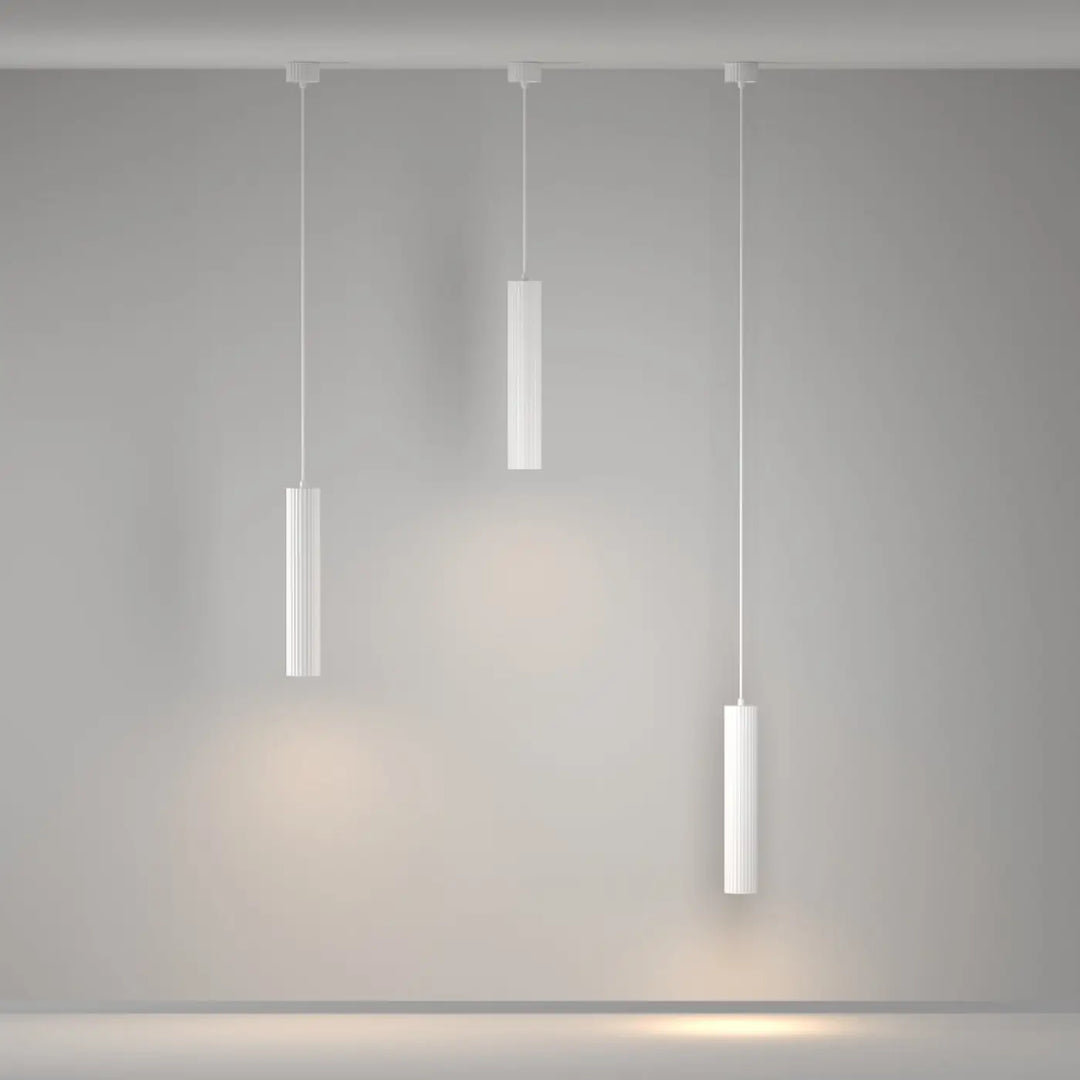 Suspension luminaire calipso tube avec trois lampes cylindriques blanches et rainurées au-dessus d’un îlot