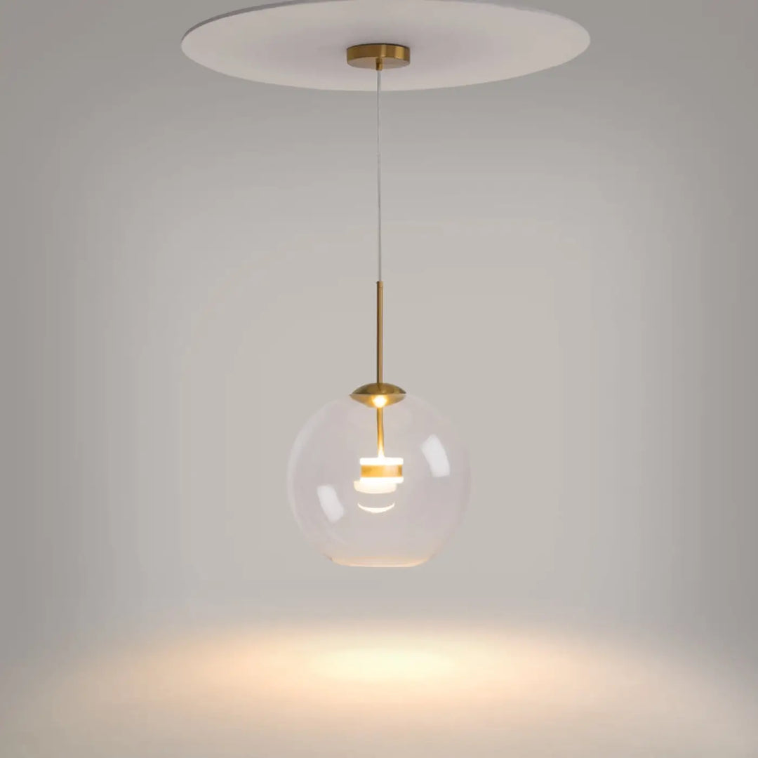 Suspension cometa en verre soufflé claire avec accents en laiton et plaque de plafond blanche au-dessus d’une table
