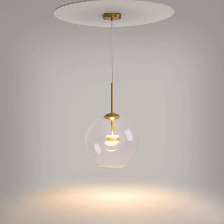 Suspension cometa en verre soufflé claire avec accents en laiton et plaque de plafond blanche au-dessus d’une table