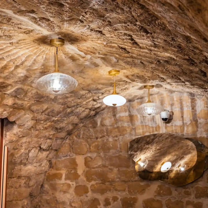 Suspension luminaire modèle grace avec trois suspensions en verre soufflé à finition laiton sous plafond en pierre rustique