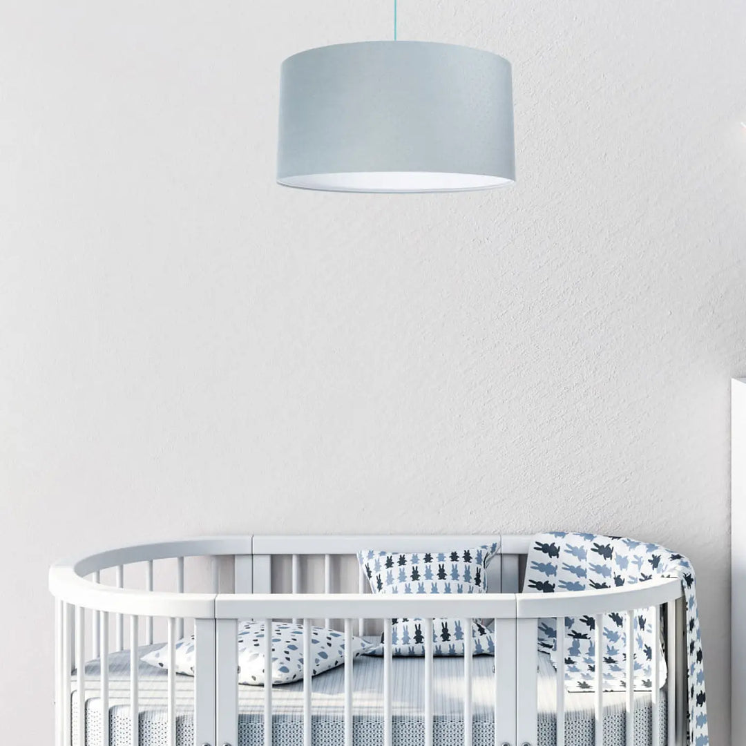 Une suspension luminaire classique jasmin bleu pastel en tissu gris cylindrique suspendue au-dessus dun lit blanc