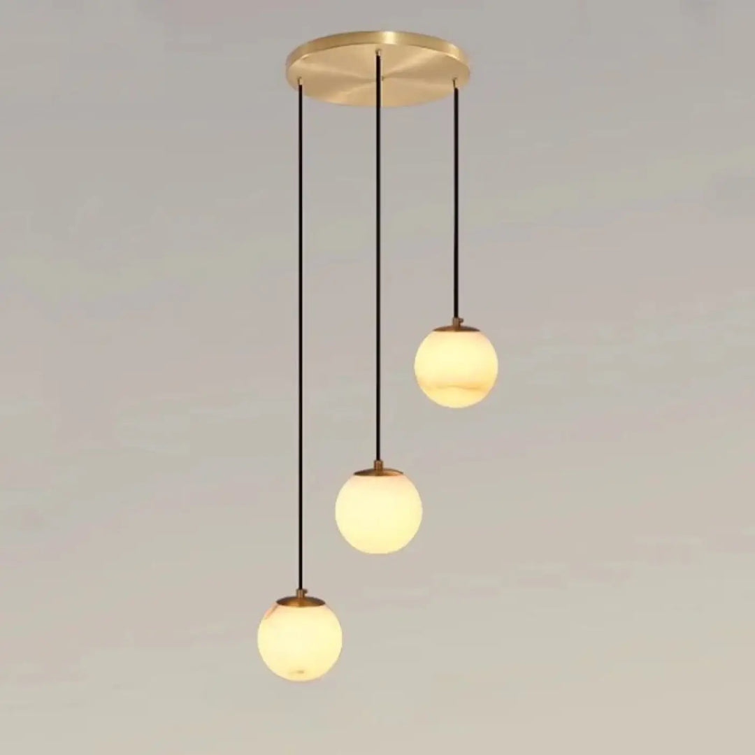 Suspension luminaire souble en laiton moderne avec trois boules en verre marbré chic suspendues par câbles noirs dans un univers art déco