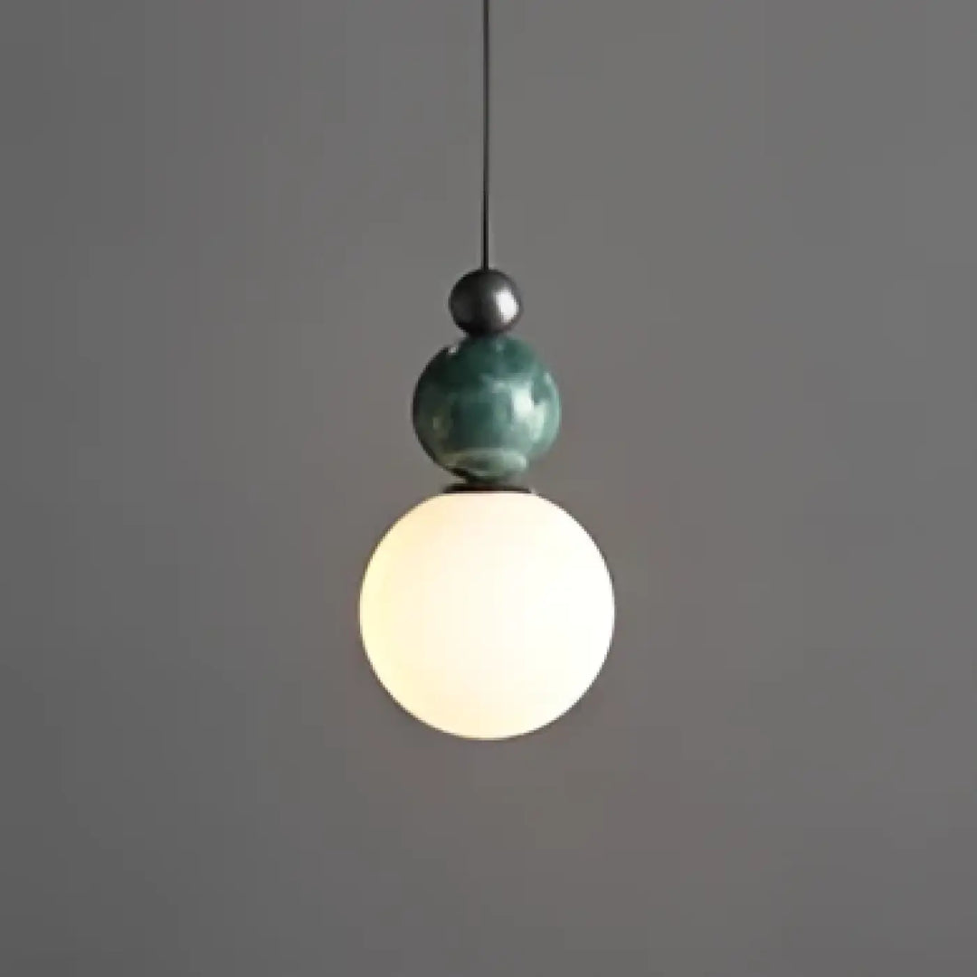 Suspension luminaire eluna avec design moderne featuring orbe céramique vert mat au-dessus d’un globe en verre blanc