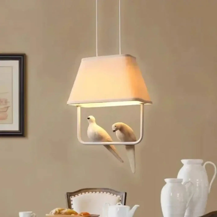 Suspension luminaire lumibird avec abat-jour en tissu blanc et cadre métallique minimaliste ornée de deux colombes sculptées